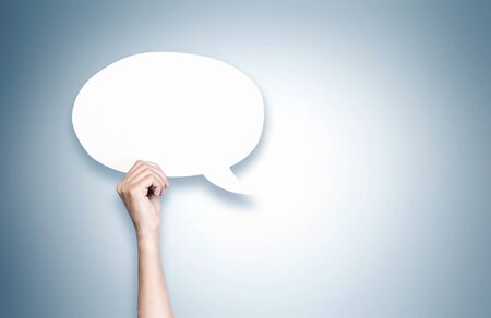 Close up of woman hand holding blank speech bubble over gray background. Concept of communication...