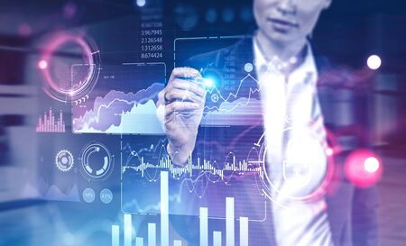 Unrecognizable young businesswoman using immersive HUD business infographic interface in blurry office. Concept of big data and hi tech. Toned imageの写真素材