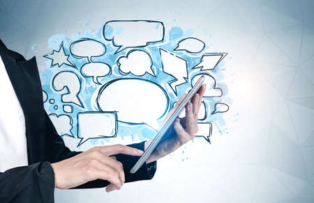Unrecognizable young woman using tablet near gray wall with empty speech bubbles drawn on it....