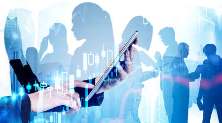 Unrecognizable businesswoman using tablet in blurry abstract city with double exposure of her team and financial graph. Concept of stock market and teamwork. Toned imageの写真素材