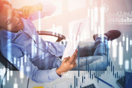 Top view of smiling young African American businessman working in blurry office with double exposure of financial graphs. Toned image.の写真素材