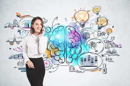 Cheerful young European businesswoman talking on smartphone near concrete wall with colorful business idea sketch. Concept of brainstormingの写真素材