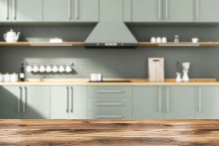 Wooden table for your product in blurry stylish kitchen with gray brick walls, gray and wooden cupboards and countertops with built in sink and cooker. 3d rendering mock upの写真素材