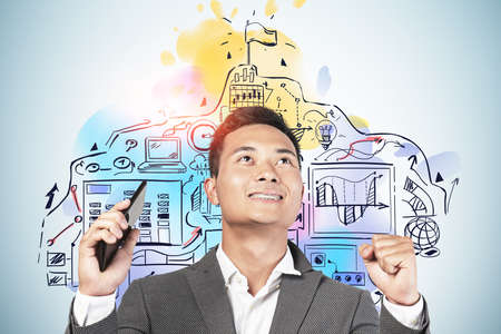 Celebrating Asian businessman holding smartphone near blue wall with creative business goal sketch...