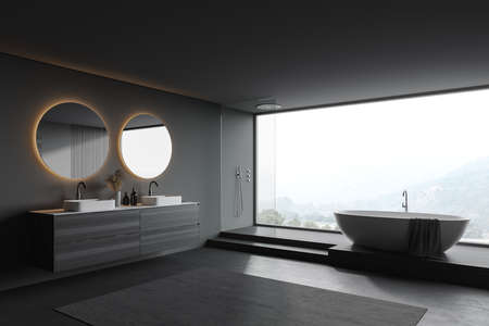 Corner of stylish panoramic bathroom with gray and wooden walls, concrete floor, comfortable tub, shower stall and double sink with round mirror. Blurry mountain view. 3d renderingの写真素材