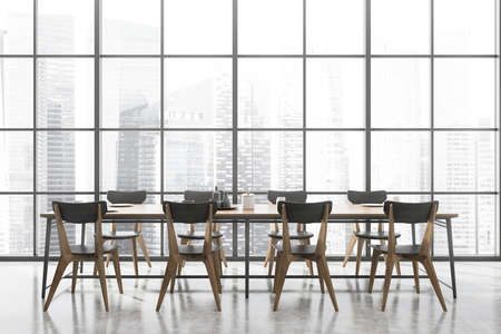 Interior of spacious panoramic dining room with concrete floor, long wooden table with gray chairs...