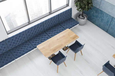 Top view of modern cafeteria with white and blue walls, wooden floor, long wooden tables with blue chairs and comfortable sofas. Window with blurry cityscape. 3d renderingの写真素材