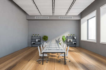 Interior of stylish open space office with gray walls, wooden floor, long white computer table with...