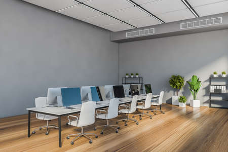 Corner of stylish open space office with gray walls, wooden floor and long white computer table with...