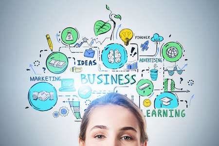 Close up portrait of smiling young businesswoman standing near gray wall with colorful business sketch drawn on itの写真素材