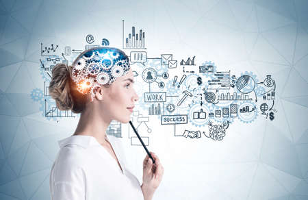 Side view of thoughtful young businesswoman with pencil standing near gray wall with brain sketch...
