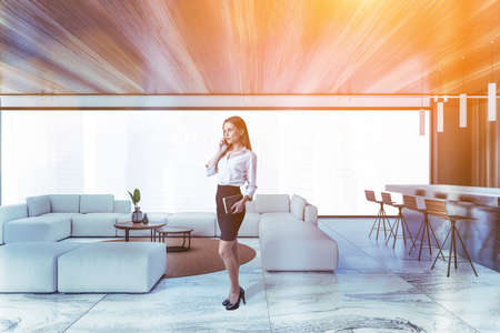 Beautiful young businesswoman talking on smartphone in luxury living room with black marble walls, bar and white sofa. Toned imageの写真素材
