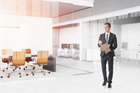 Confident young businessman with clipboard walking in modern office. Concept of management. Toned...