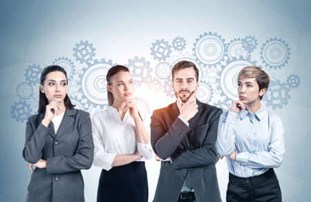 Successful young business team members standing near gray wall with gears drawn on it. Concept of...