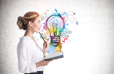 Side view of thoughtful young businesswoman with notebook standing near concrete wall with bright idea sketch. Mock upの写真素材