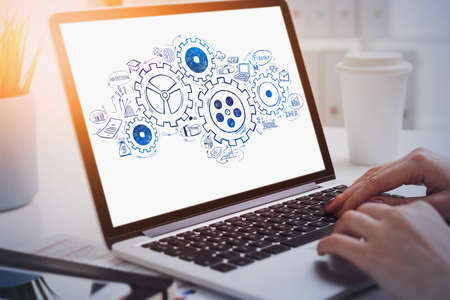 Hands of businesswoman using laptop on table with gears sketch drawn on screen. Concept of teamwork....
