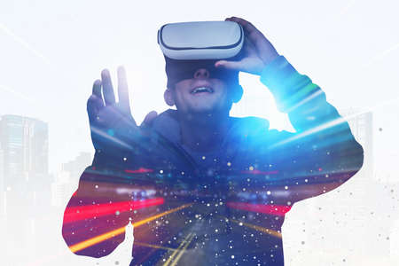 Portrait of young man in gray shirt using virtual reality glasses and gesturing in blurry night city...