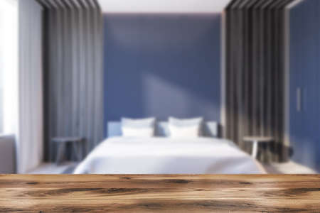 Wooden table for your product in blurry master bedroom with blue and gray walls, concrete floor and...