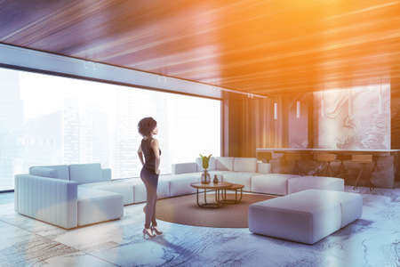Young African American woman standing in luxury living room with black marble walls, panoramic...