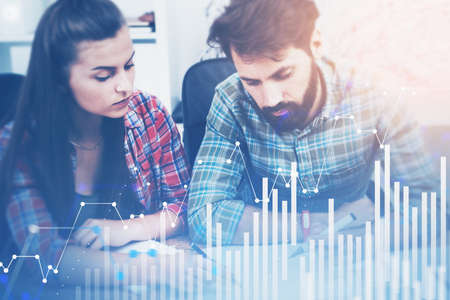 Businessman and businesswoman working in blurry office with double exposure of digital charts. Toned imageの写真素材