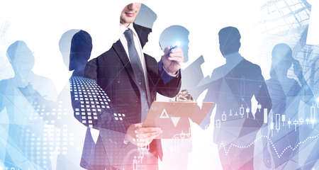 Young businessman with clipboard standing in blurry city with double exposure of digital charts and...