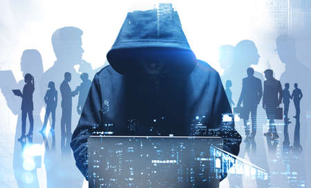 Unrecognizable young hacker in hoodie using laptop in blurry night city. Business people. Concept of cybersecurity. Toned image double expsoureの写真素材