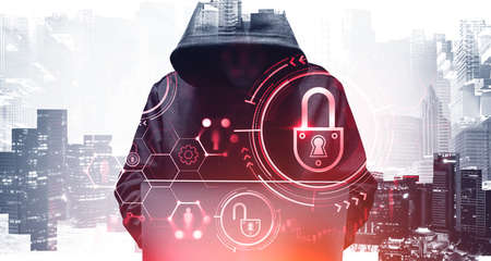 Unrecognizable young hacker in hoodie using laptop in blurry city. Concept of cybersecurity. Toned...