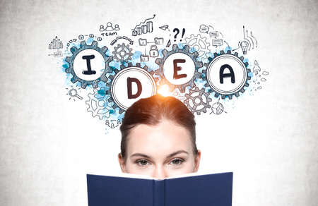 Young businesswoman with book standing near concrete wall with business idea sketch drawn on it.