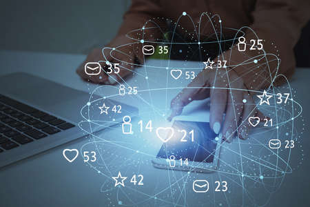 Hand of businesswoman using smartphone and laptop in blurry office with double exposure of social...
