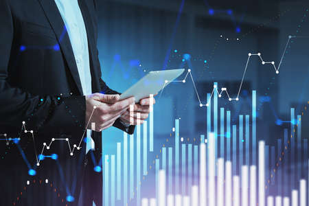 Unrecognizable businessman using tablet in blurry office with double exposure of digital charts. Toned imageの写真素材