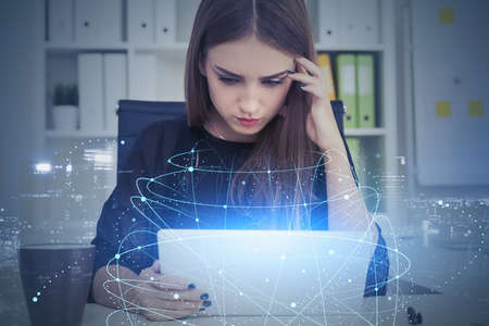Serious young businesswoman using tablet in blurry office with double exposure of network interface....