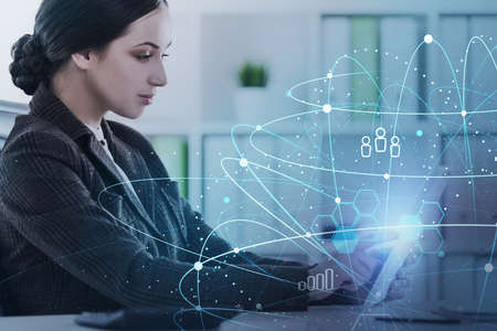 Serious young businesswoman using laptop in blurry office with double exposure of network interface....