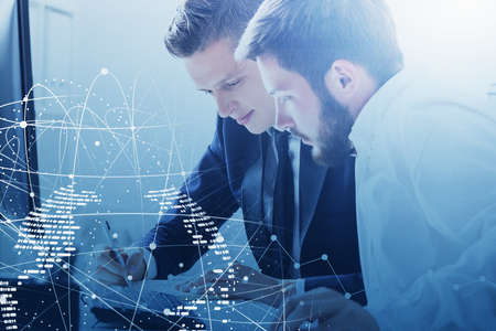 Portrait of two young businessmen working with laptop in blurry office with double exposure of...