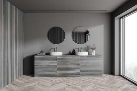 Interior of modern bathroom with gray walls, wooden floor, double sink and two round mirrors. Window...
