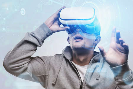 Young man in VR glasses standing over blurry night cityscape background with double exposure of...