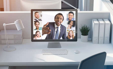 Cheerful young African American businessman having video conference with his diverse colleagues. Modern computer on white table. Concept of working from home during covid 19 pandemicの写真素材