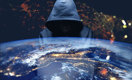 Unrecognizable hacker using laptop over Earth background. Toned image double exposure.
