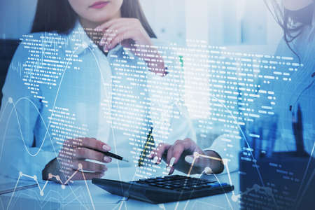 Unrecognizable young businesswoman working in blurry office with double exposure of financial graph...