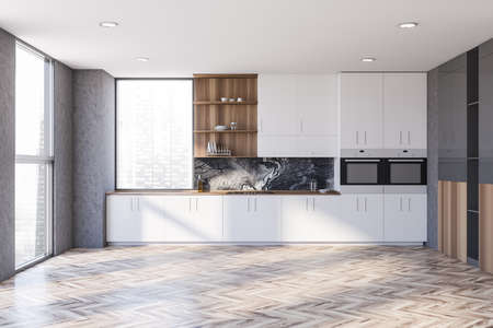Interior of stylish kitchen with concrete walls, wooden floor and white cabinets with built in sink...