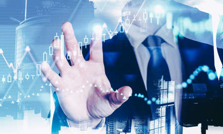 Businessman hand using financial graph interface over blurry cityscape background. Toned image double exposureの写真素材