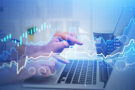 Hands of businessman typing on laptop in blurry office with double exposure of financial graph....