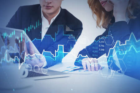 Businesswoman and businessman working in blurry office with double exposure of financial graph....