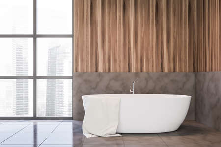 Interior of stylish bathroom with gray and wooden walls and floor, window with blurry cityscape and comfortable bathtub. 3d renderingの写真素材