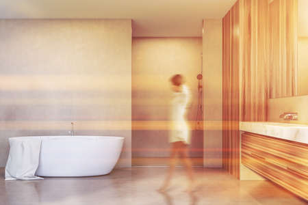 Blurry young woman walking in modern bathroom with white and wooden walls, concrete floor, shower stall, tub and double sink. Toned imageの写真素材