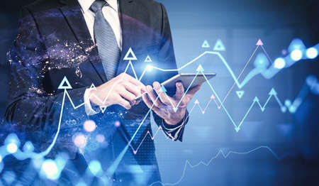 Unrecognizable businessman using tablet in blurry office with double exposure of graphs and planet...