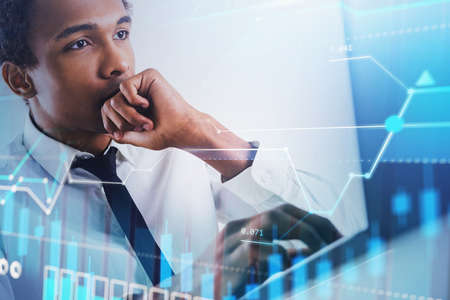 Serious young African American businessman working in blurry office with double exposure of...