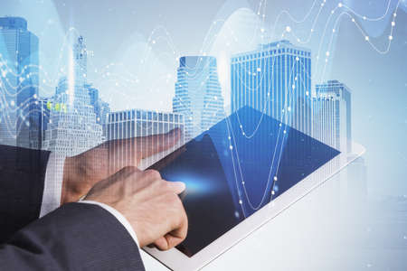 Hands of businessman using tablet computer in blurry city with dobule exposure of financial graph....