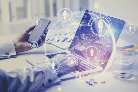 Hands of businessman using laptop and smartphone in blurry office with double exposure of HR...