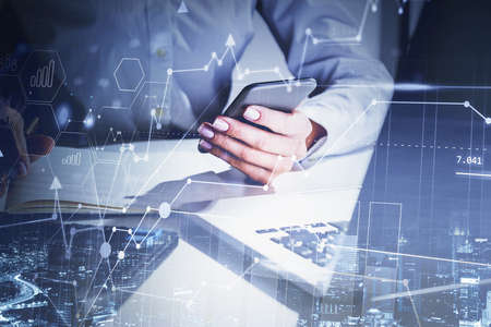 Hands of businesswoman using smartphone in blurry office with double exposure of financial graphs. Toned imageの写真素材