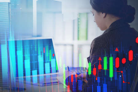 Young businesswoman working with laptop in blurry office with double exposure of financial graph....